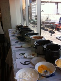 a long table topped with lots of bowls and pans filled with food next to windows