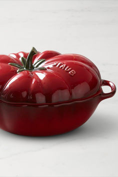 a red ceramic casserole dish with a tomato on the top, sitting on a white countertop