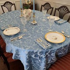 a blue table cloth with white plates and silverware on it in a dining room