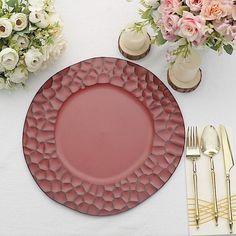 a pink plate sitting on top of a white table next to silverware and flowers