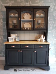 a black china cabinet with glass doors and plates on the top, in front of a wallpapered background