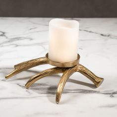 a candle holder made out of brass antlers on a marble countertop with a white lit candle in the middle