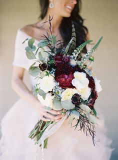 a woman in a white dress holding a bouquet of flowers and greenery on her wedding day