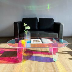 a glass coffee table sitting on top of a wooden floor next to a black couch