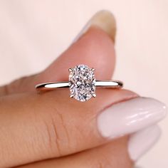 a woman's hand holding a ring with a large diamond in the center and a white manicured nail