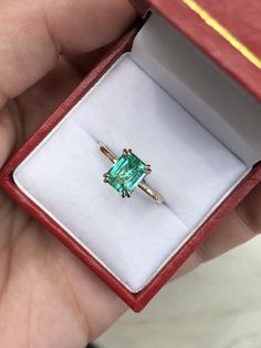 someone is holding an emerald ring in a red box with gold trimmings on it