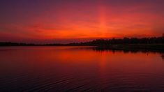 the sun is setting over water with trees in the background