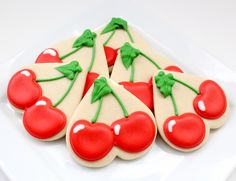 four decorated cherry cookies on a white plate with green leaves and red cherries in the middle