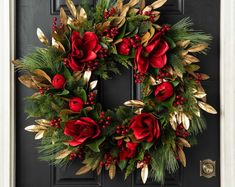 a wreath with red flowers and greenery is hanging on a black front door,