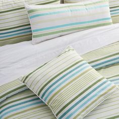 a bed with green and blue striped pillows on it's headboard, next to a white comforter