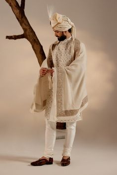 Turtle Dove Sherwani Set | Jatin Malik Introducing our renowned Kashmiri Jamawar embroidered sherwani, crafted in a captivating dirty ivory hue and adorned with intricate floral design details. This masterpiece is further elevated with exquisite dabka and zari work, adding a touch of opulence and refinement. Paired with a matching Ladakhi Pashmina shawl and safa, this ensemble exudes timeless elegance and sophistication, perfect for special occasions and celebrations. With its impeccable craftsmanship and attention to detail, this sherwani set is sure to make a memorable statement. Included in purchase: Sherwani, Kurta, Churidar, Pashmina Shawl, Safa Product Specification Color: White Fabric: Linen silk Occasion: Engagement, Wedding, Bridal, Reception Style: Sherwani, Kurta, Churidar, Pash Off White Traditional Wear With Dabka For Designer Occasions, Off White Naqshi Traditional Wear For Festive Occasions, Off White Bandhgala With Naqshi For Festive Occasions, Off White Naqshi Bandhgala For Festive Occasions, Festive Eid Sherwani With Chikankari Embroidery, Traditional Off-white Kurta With Naqshi, Traditional Off White Kurta With Naqshi, Designer Traditional Drape Off White Kurta, Off White Kurta With Dupatta In Traditional Drape