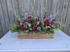 a wooden box filled with flowers and greenery on top of a blue table next to a fence