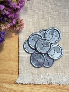 six metal buttons sitting on top of a table next to some purple and white flowers