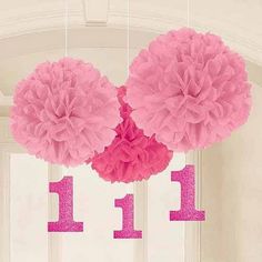 three pink tissue pom poms hanging from the ceiling in front of a window