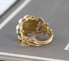 "An immaculate antique Georgian mourning ring, crafted in 18k yellow gold with a lustrous split pearl halo around the center compartment which holds a momento of woven hair under crystal. The shoulders are delicately articulated in a baroque scroll design, accented by glossy black enamel, and the ring is fully hallmarked for 18k, London manufacture, and letter dated 1828. Measuring approximately 1/2\" north to south at the center front, tapering through the shoulders to 2.22 mm at the center bac Formal Yellow Gold Pearl Ring With Rose Cut Diamonds, Victorian Gold Cameo Rings, Antique Open Ring Wedding Jewelry, Antique Yellow Gold Pearl Ring With Rose Cut Diamonds, Antique Open Ring Jewelry For Wedding, Heirloom Pearl Open Ring For Formal Occasions, Heirloom Style Pearl Open Ring For Formal Occasions, Heirloom Style Formal Pearl Open Ring, Formal Heirloom Pearl Open Ring