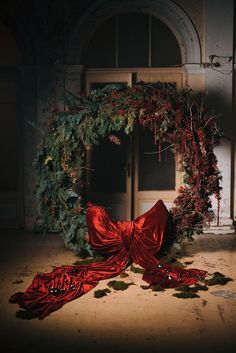 a christmas wreath with red ribbon laying on the ground in front of an open door