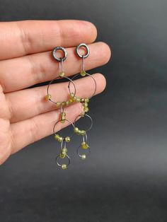 a hand holding three small silver and green beaded hoop earrings on it's fingers