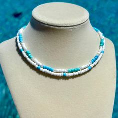 a white and blue beaded necklace is on a mannequin head stand in front of a swimming pool