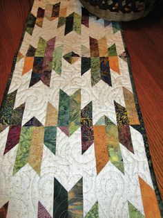 a quilted table runner with an arrow design on the top and bottom, sitting on a wooden floor