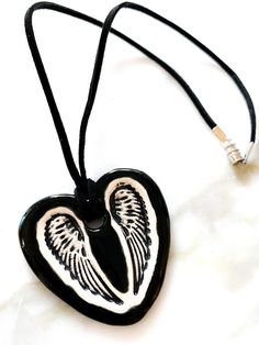 This is a hand-formed and hand painted ceramic heart with wings necklace made by Surly Amy at Surly-Ramics. This necklace has one of our small size pendants.*PLEASE NOTE I make these in small batches so the necklace you receive may vary slightly from the one in the photo. The color, size and style will be the same but the glaze will settle slightly differently from piece to piece.I have posted some photos of one of my models the beautiful Surly Brooke wearing a similar necklace so you can see ho Black Heart-shaped Necklace For Keepsake, Black Heart Necklace For Keepsake, Black Heart Necklaces For Keepsake, Gift Black Jewelry With Wing-shaped Pendant, Wing-shaped Black Jewelry Gift, Wing-shaped Black Jewelry For Gifts, Black Wing-shaped Jewelry Gift, Black Wing-shaped Jewelry For Gifts, Hand Painted White Heart Jewelry