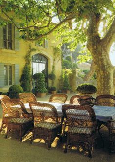 an outdoor dining table and chairs in front of a large yellow building with trees around it