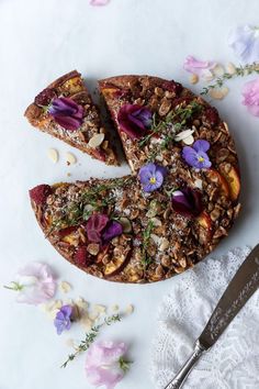 a cake with flowers and nuts on it next to a knife, fork and napkin