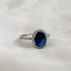 an oval blue stone surrounded by diamonds on a white cloth with a ring in the middle