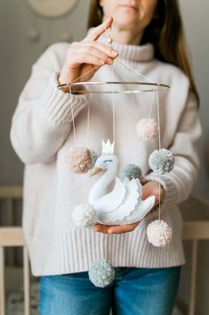 a woman holding a swan mobile with pom poms