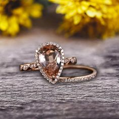 an engagement ring with a pear shaped morganite surrounded by small diamonds on a wooden surface