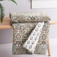 a close up of a blanket on a chair with a plant in the corner behind it