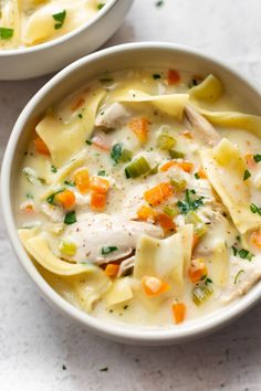 two bowls filled with chicken noodle soup on top of a white countertop next to each other