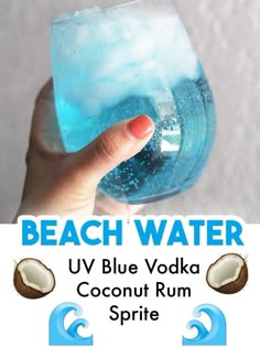 a hand holding a glass filled with blue vodka and coconut sprite next to a sign that says beach water