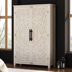 an ornate white armoire in a black room with wood flooring and large windows