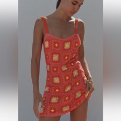 a woman in an orange crochet swimsuit is standing on the beach and looking down