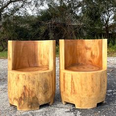 two wooden chairs sitting next to each other on top of a gravel field with trees in the background