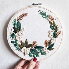 a hand is holding a embroidery hoop with white flowers and green leaves