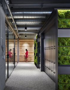 an office hallway with green walls and metal lockers on both sides, two women in red dresses are walking down the corridor