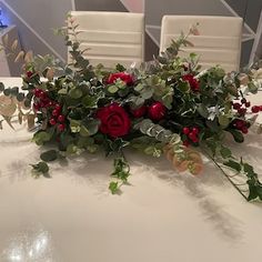 a white table topped with red flowers and greenery