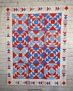 a red, white and blue quilt hanging on a brick wall