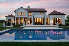 a large house with a pool in front of it at dusk or dawn, as seen from across the yard