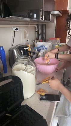 two people in the kitchen mixing ingredients for some kind of cake batter or ice cream