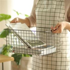 a woman holding a wire basket with magazines in it