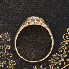 a gold ring with two diamonds sitting on top of a black cloth next to an ornate design