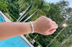 a person wearing a bracelet next to a swimming pool with trees and bushes in the background