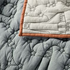 an airplane quilted on top of a bed with orange trimmings and white sheets