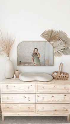 a dresser with a mirror and vases on it in front of a white wall