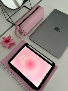 an apple laptop computer sitting on top of a table next to a pink bag and notebook