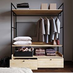 an open closet with clothes and shoes on shelves next to a bed in a bedroom