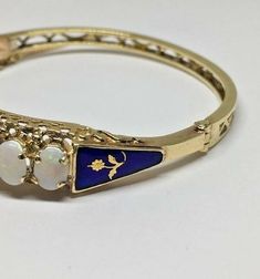 Estate 9 Oval Opal Royal Blue Floral Flower Enamel Hinged 14k YG Bangle BraceletMaterial: 14k yellow gold, stampedWeight: 18.5 gramsDiameter: 2 1/2"Size: 10mm wide (top of bracelet)2 3/4" long (safety chain)Stones: 9 oval opals 7 x 5mm each (all opals are slightly over 7 x 5mm), all in perfect conditionRoyal blue enamel on both sides with a flower design in centerAll original enamel in perfect conditionHallmarked: 14k This is an estate piece in excellent condition, it is in it's original worn st Heirloom 14k Gold Round Bracelets, Heirloom 14k Gold Round Bracelet, Heirloom 14k Gold Bracelets, Yellow Gold Multi-stone Oval Bracelet, Yellow Gold Multi-stone Oval Bracelets, Yellow Gold Oval Bracelet With Multi-stone, Yellow Gold Oval Multi-stone Bracelet, Heirloom 14k Stamped Jewelry Bangle, Gold Oval Bracelet Stamped 14k