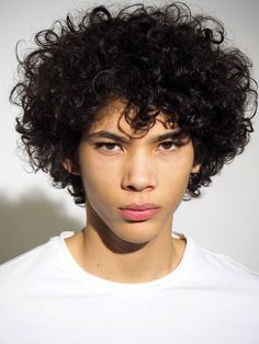 a close up of a person wearing a white t - shirt and short curly hair